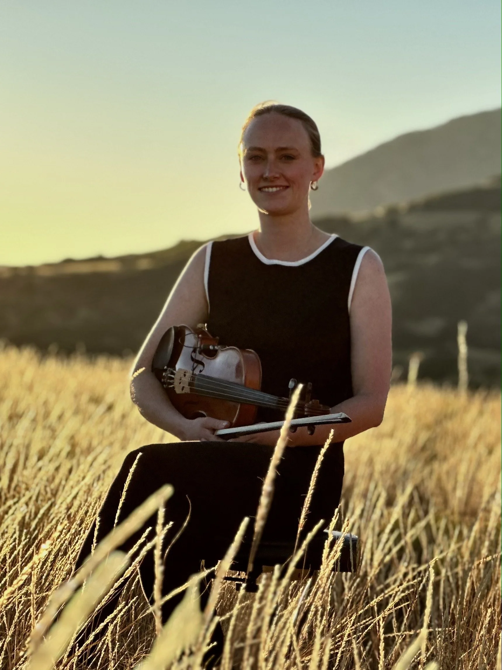 Annie Foxen holding a violin in a golden Telluride field at sunset